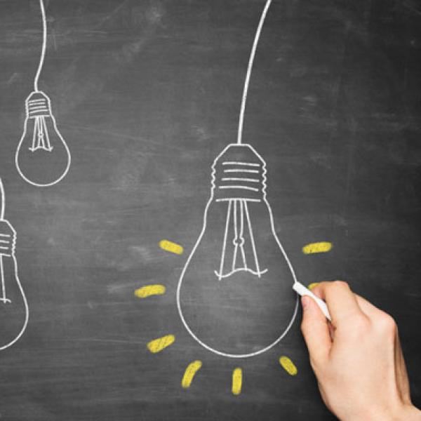 A hand drawing light bulbs on blackboard.