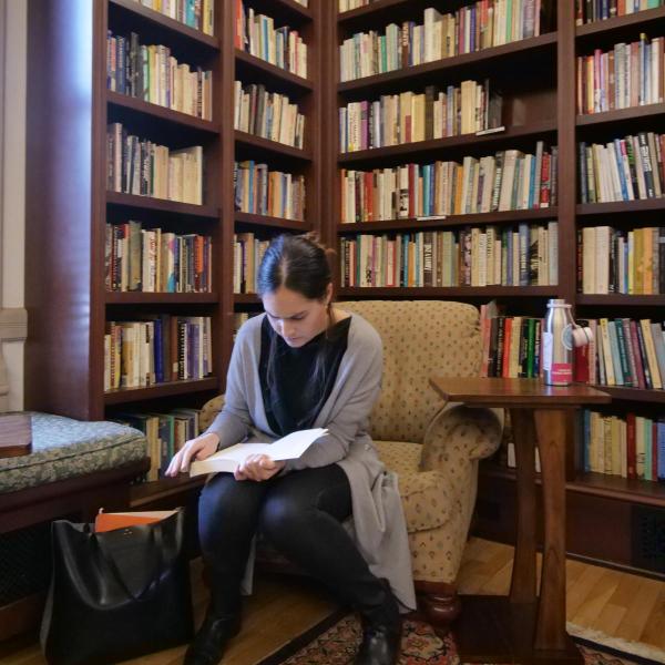 A student sits in a library room reading surrounded by books