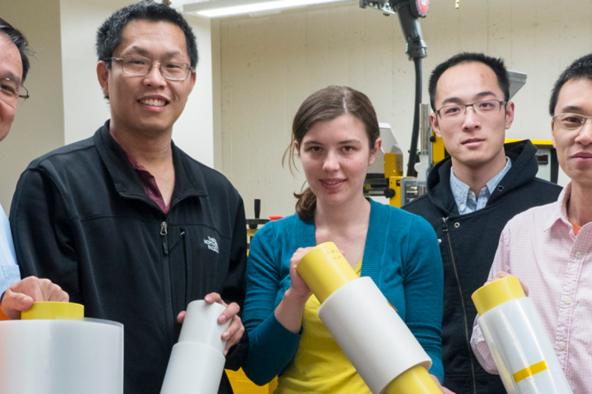Ronggui Yang and Xiaobo Yin in a lab with a group of students holding rolls of a film material.