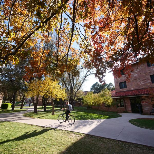 a student rides a bike past the Kittredge residence hall with fall foliage surrounding