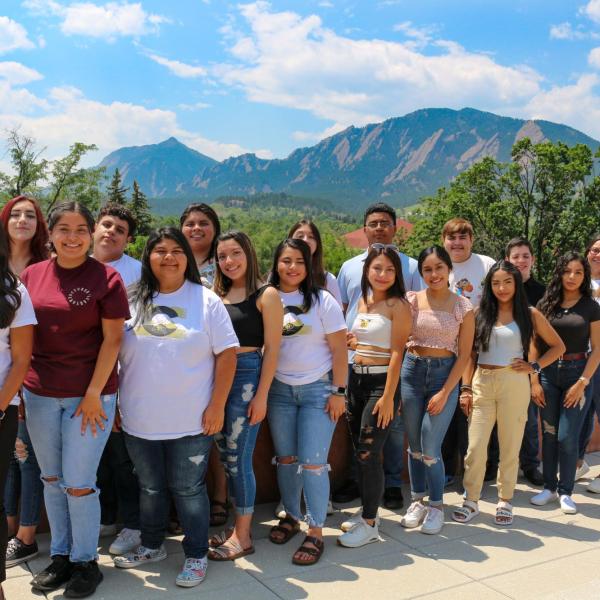 a group of Boulder county precollege students stand on the roof of the CASE building with the flatirons visible behind them