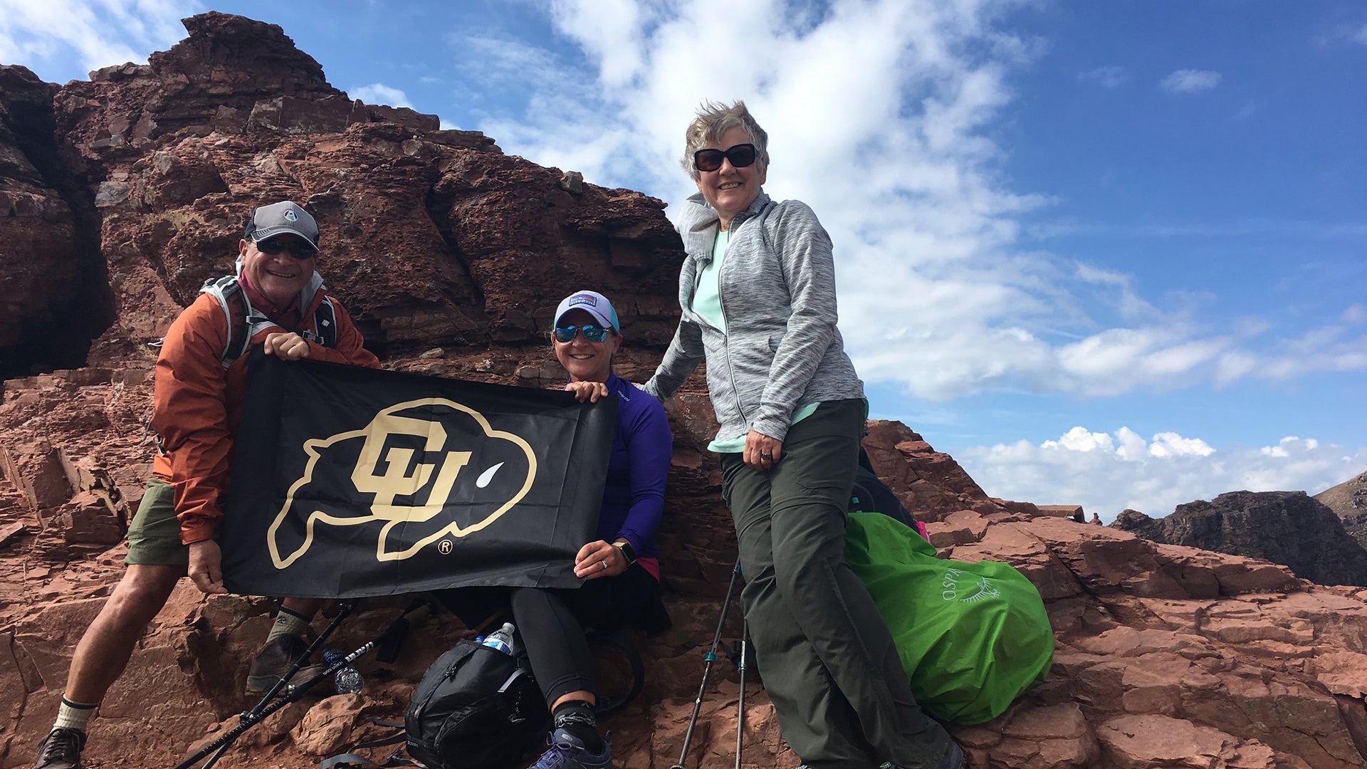 A group of alumni with a CU Bouder flag on a mountaintop