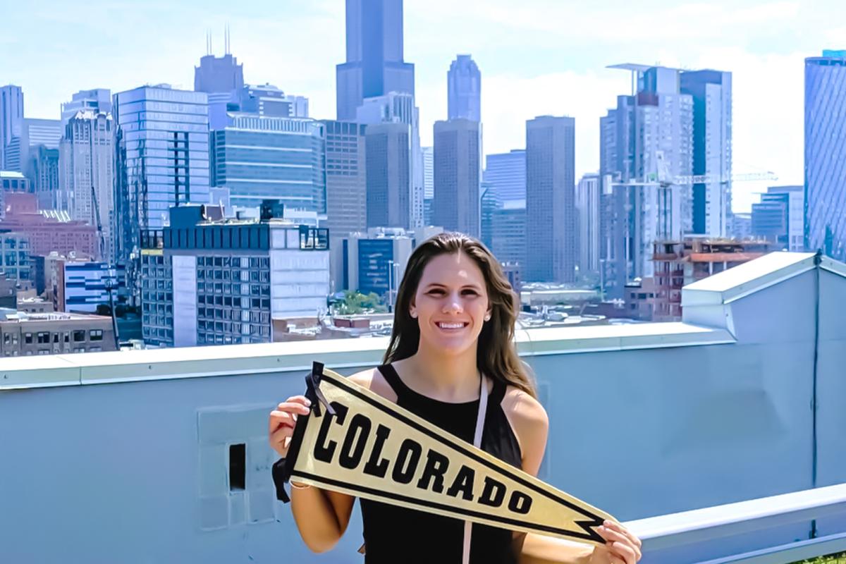 alumni holding Colorado pennant in front of skyline