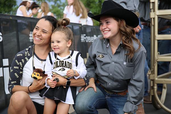 young family and CU Boulder fans pose with one of Ralphie's handlers