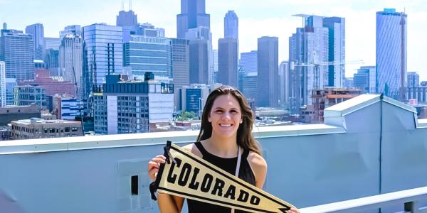 alumni holding Colorado pennant in front of skyline