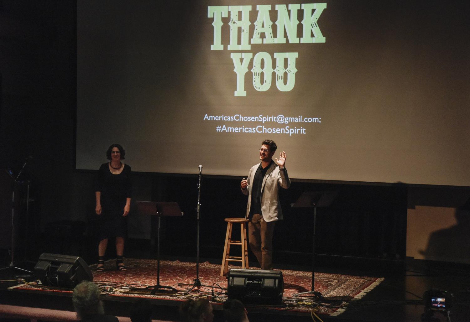 Janice Fernheimer and JT Waldman standing on stage, a "thank you" on the screen behind them