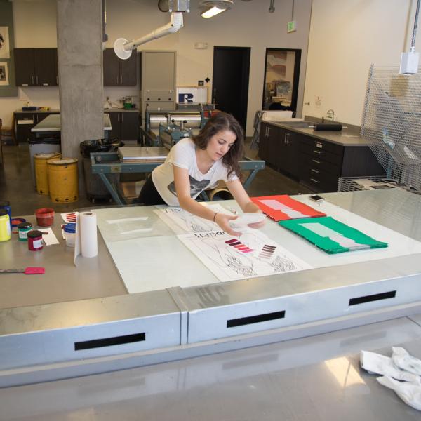 A printmaking student prepares materials and ink in the classroom for a project.