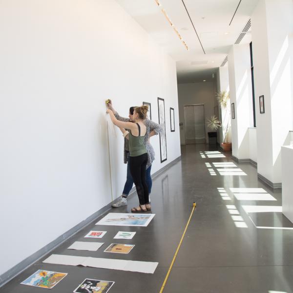 Students hanging artwork in the exhibition space on the third floor