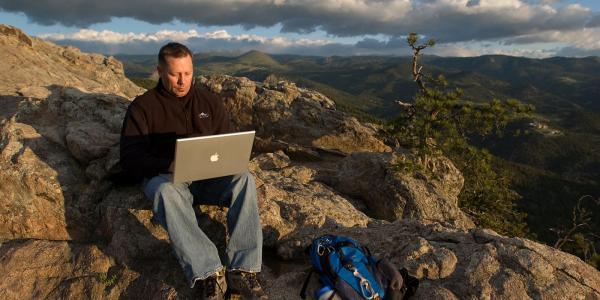 student with computer in scenic Boulder Colorado mountains