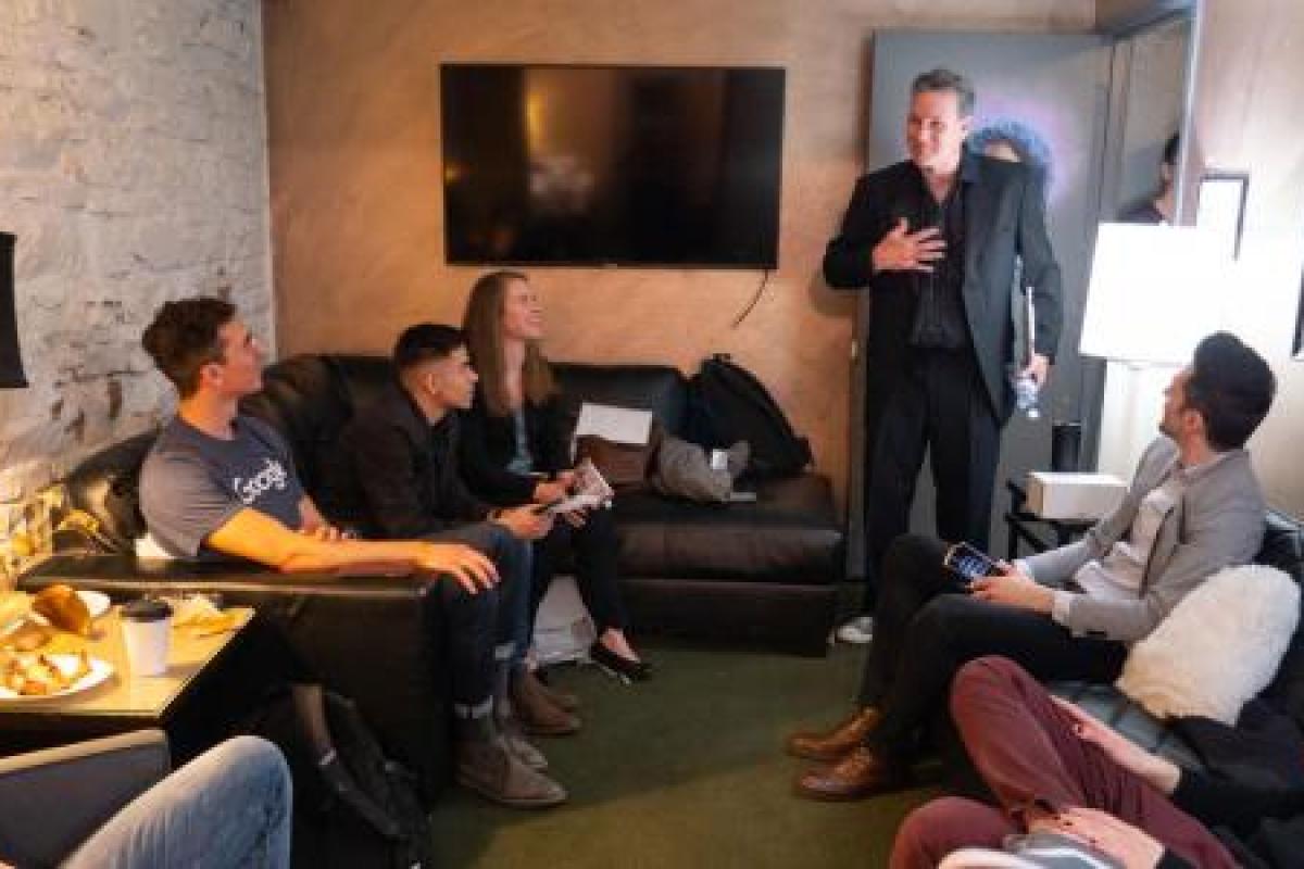 Students sit in a faculty members' living room, listening to a lecture