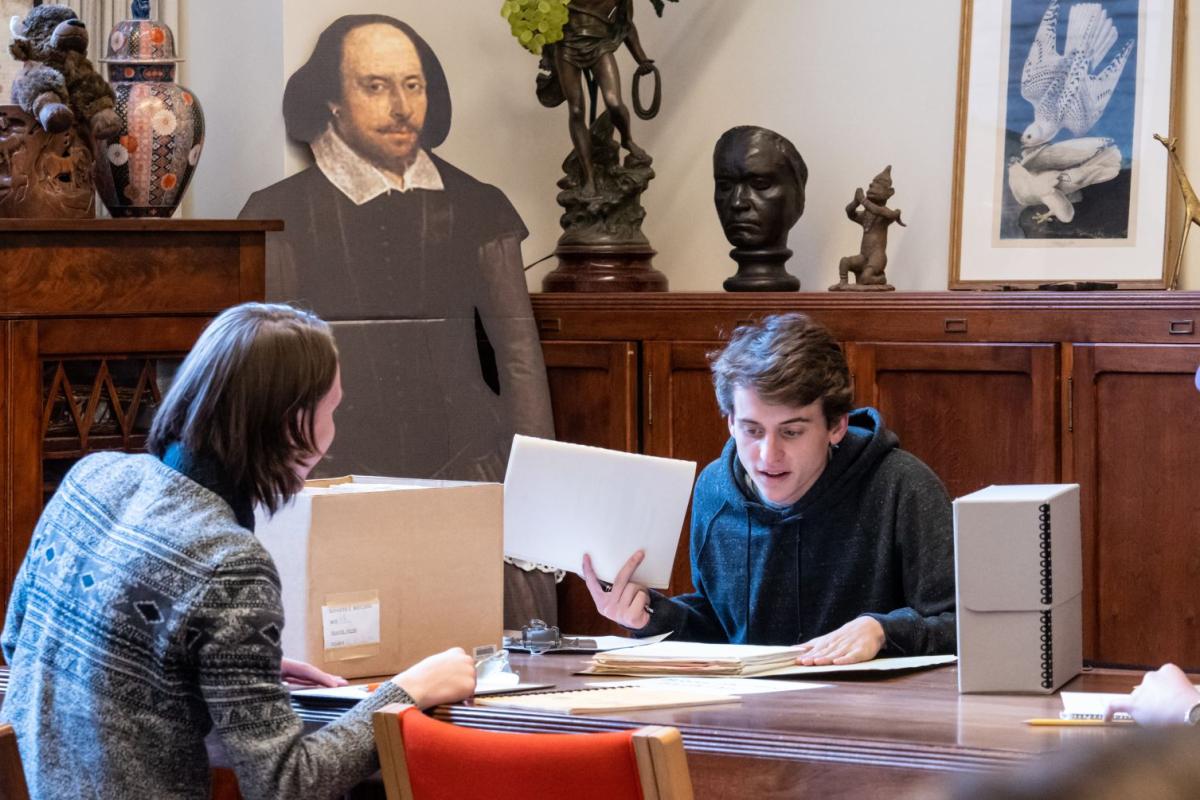 Two students look at historical texts while a cutout of William Shakespeare looks on.