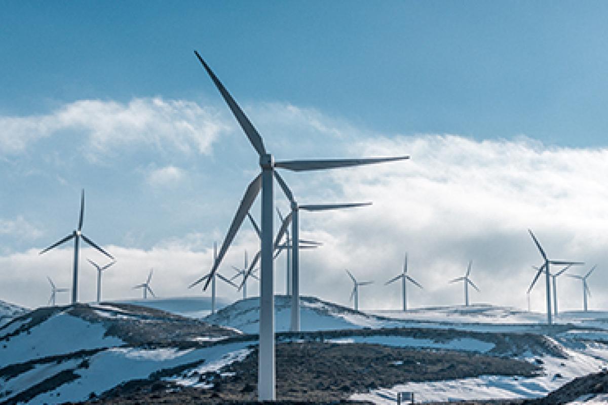 A series of wind farm fans are seen against a snowy, blue sky.