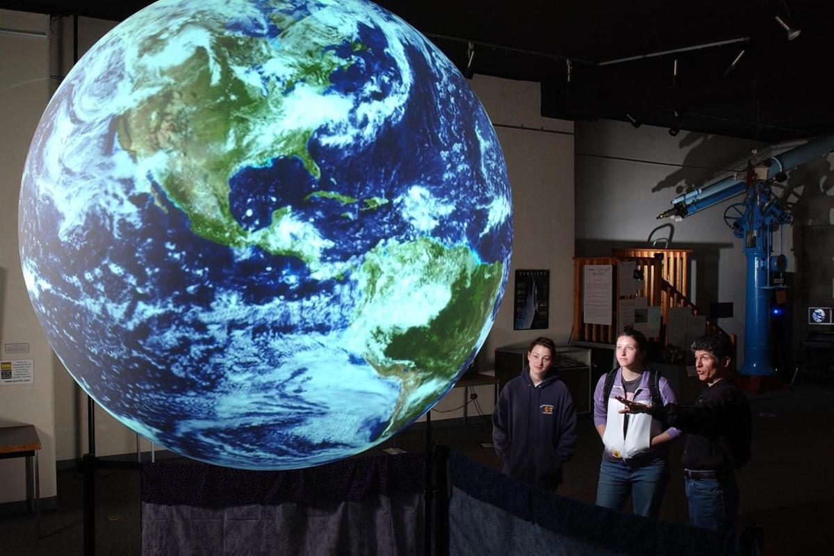 Two students look at a globe while a faculty member explains a weather pattern
