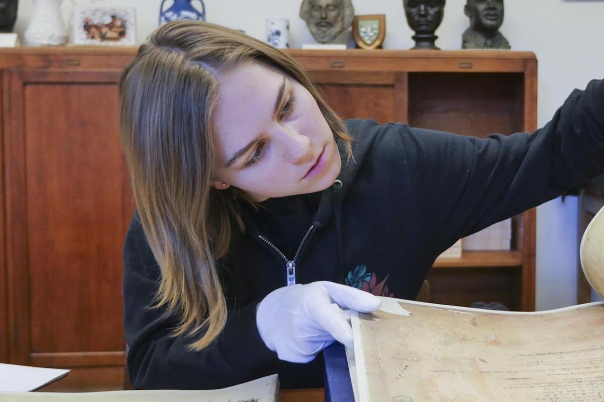 A student wearing protective gloves analyzes a historic text.