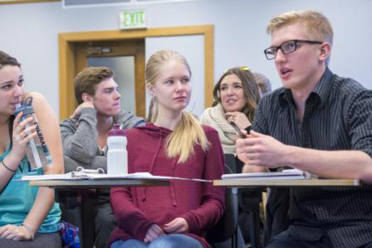 Three students discuss a concept in a small lecture classroom.