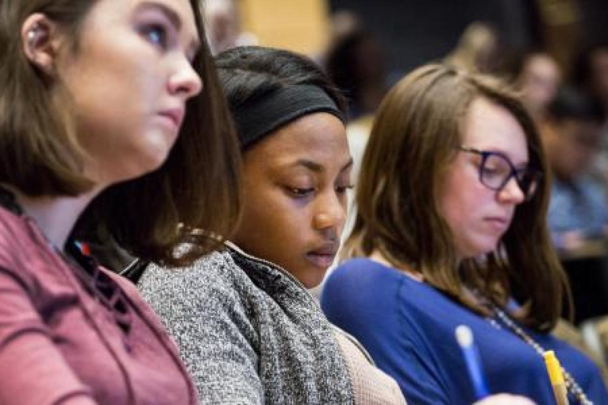 Three students listen to a lecture and take notes.