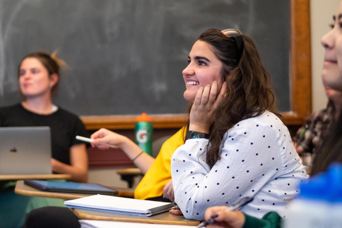 A student smiles while looking ahead at a lecture presentation