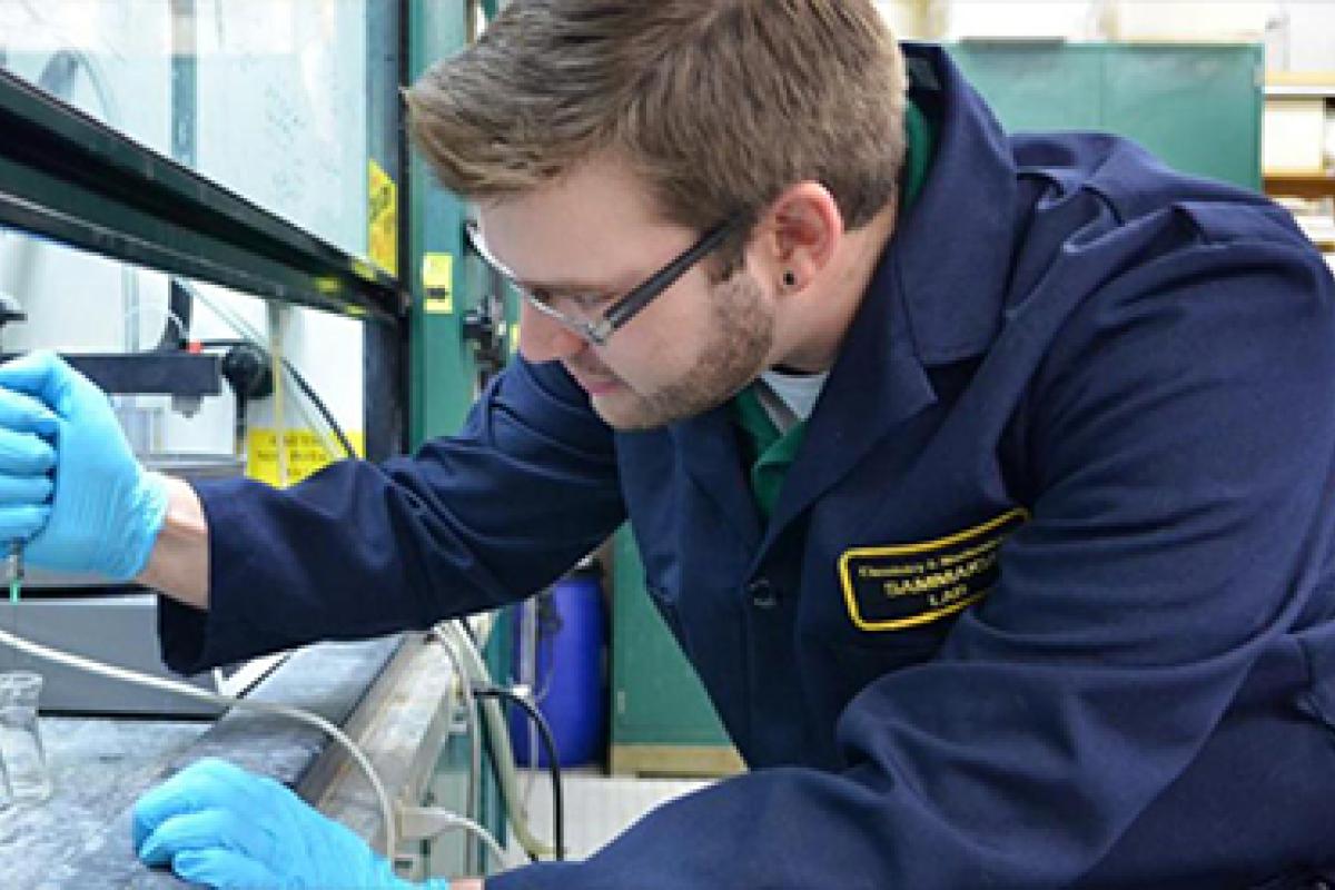 A student in lab dress and protective gloves drops a liquid into a series of petri dishes