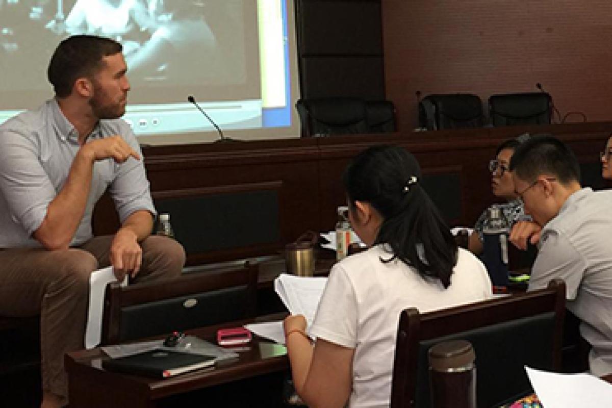 A linguistics faculty who is sitting on a desk leads a small group discussion.