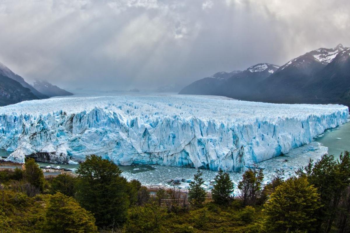 A melting glacier stands in a wide bay with high mountains in the background