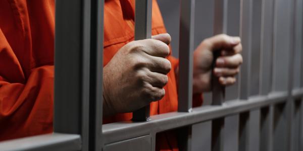 Man in orange jumpsuit holding prison bars