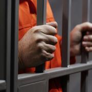 Man in orange jumpsuit holding prison bars