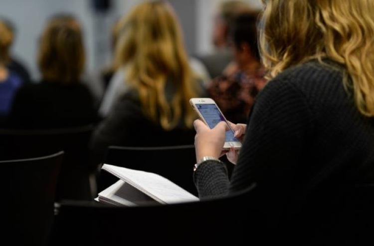 Female student using a mobile phone in a large lecture class