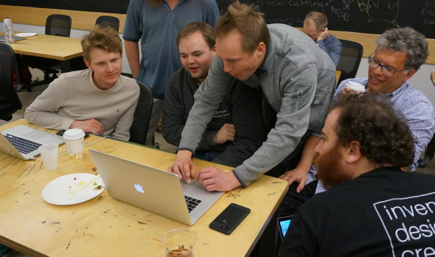 Tom Ball demonstrates MakeCode on his computer,  surrounded by workshop participants.