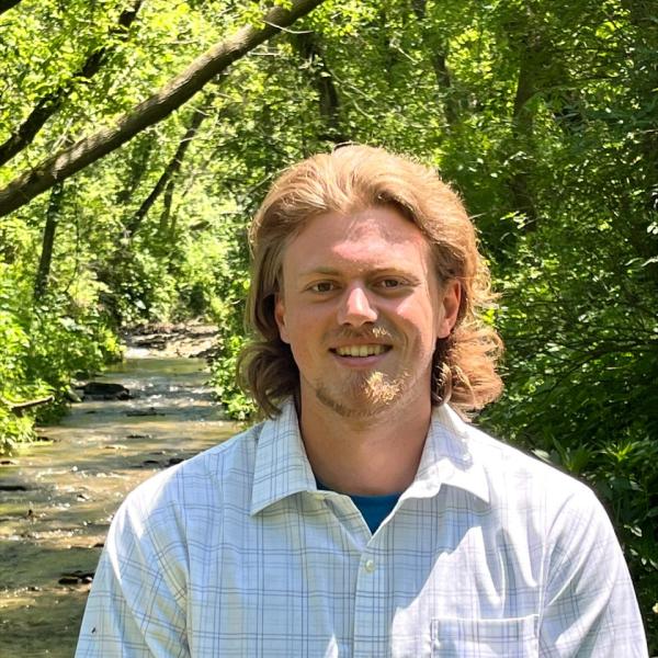 Nathan Clarke stands on a trail with trees behind him.