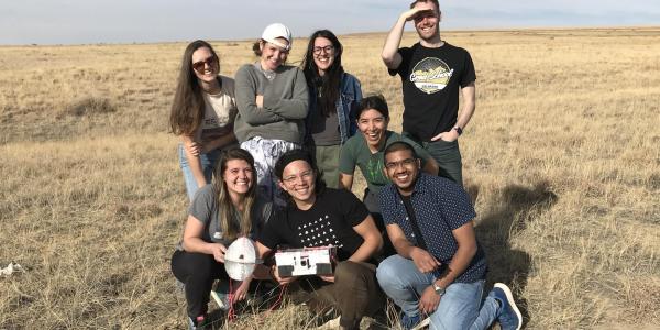 Students pose in field with flight control unit after retrieving it in Eastern Colorado.