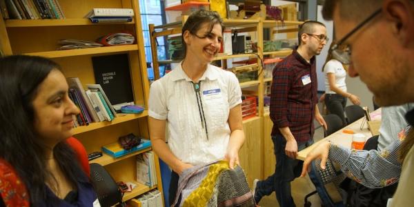 Laura Devendorf stands smiling in the Unstable Design Lab while holding a colorful woven form and showing it to guests