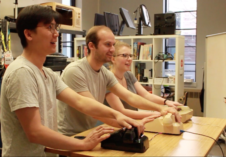 Three players with hands on analog phones play the game Buy! Sell!.