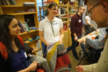 Laura Devendorf stands smiling in the Unstable Design Lab while holding a colorful woven form and showing it to guests