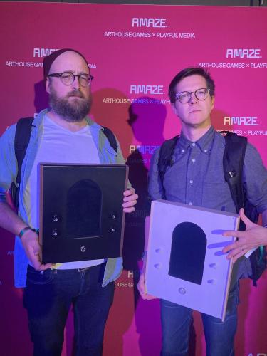 two men holding synthesizers in front of a pink background that says AMAZE