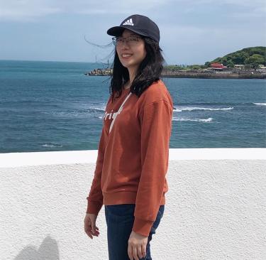 Chin-Hsuan Wang in front of a short wall with the ocean behind her.