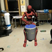 Torin Hopkins beats on a drum next to an avatar also beating on a drum