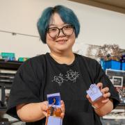 Ruhan stands in the ACME Lab holding examples of her paper robots