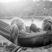 The back of heads of two young girls in a hammock by a lake.