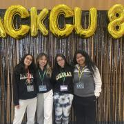 Hack CU winners stand on stage below balloons spelling "HackCU."