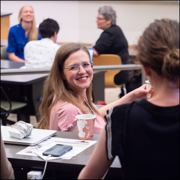 A woman smiling behind her shoulder at another woman with a group of three people talking together in the background