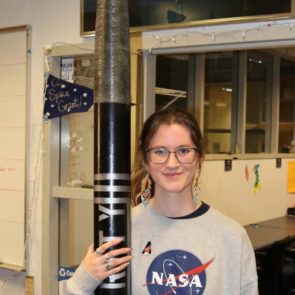 Evie Clarke wearing a NASA sweatshirt and standing with a model rocket