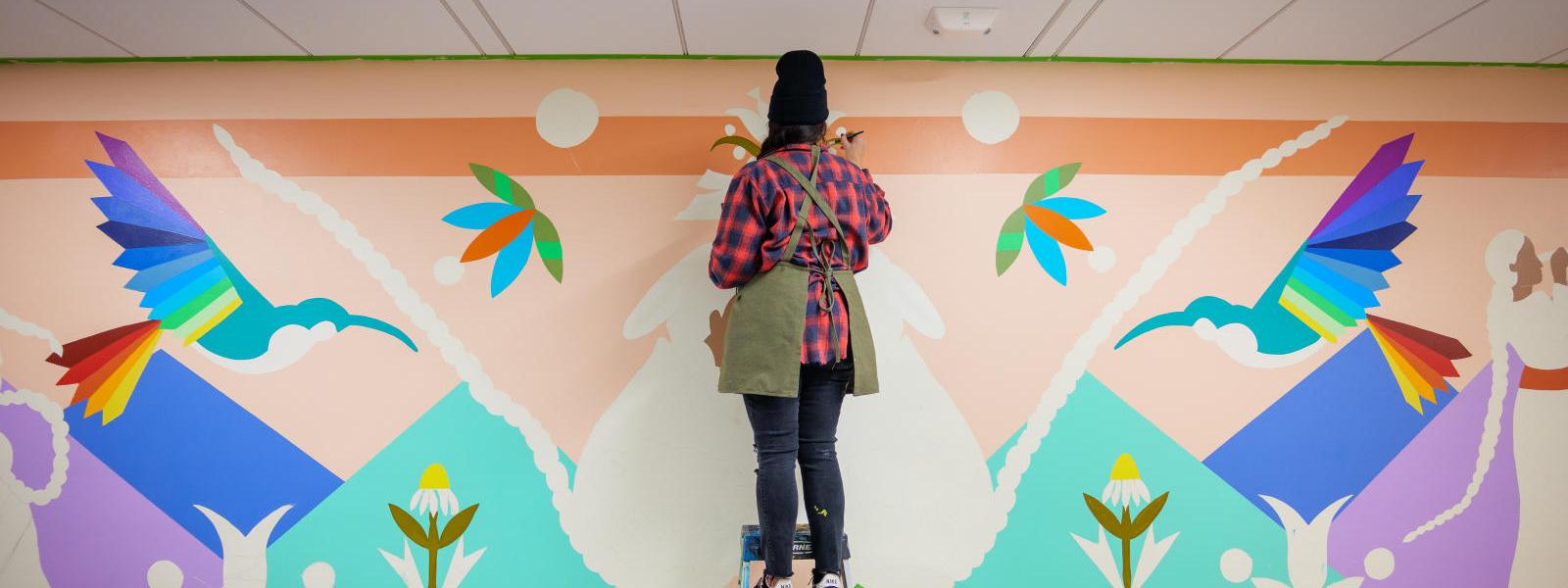 Artist Danielle SeeWalker paints a mural at the Miramontes Baca Education Building.