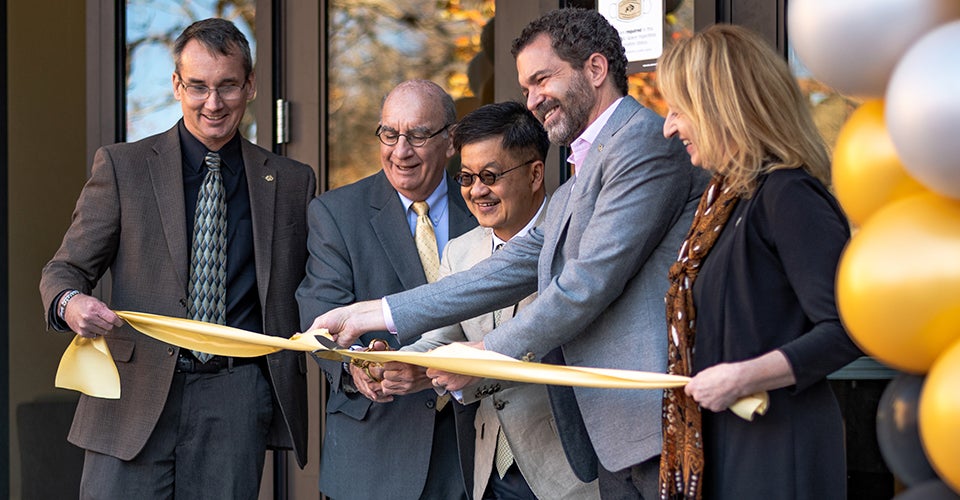 Five people in professional dress cut the ribbon on a new building on the CU Boulder campus.