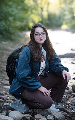 Julie Gentile kneels beside a creek in the middle of the woods.