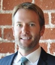 Headshot of Brad Rable in a blue suit against a brick wall.
