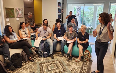 A female professor leads a group discussion in a crowded room.