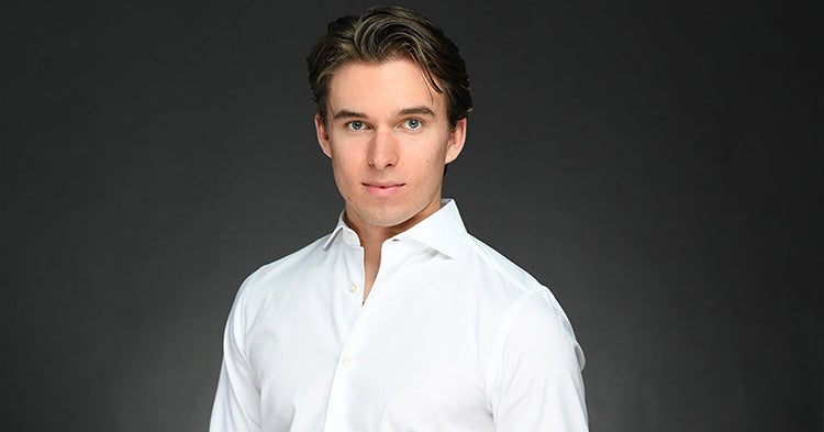 Professional headshot of Ronan in a white dress shirt against a dark background.