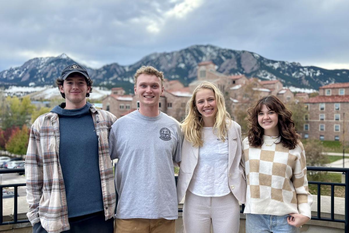 Four Sustainability Scholars undergraduate students smiling on the CU Boulder campus with the Flatirons in the background