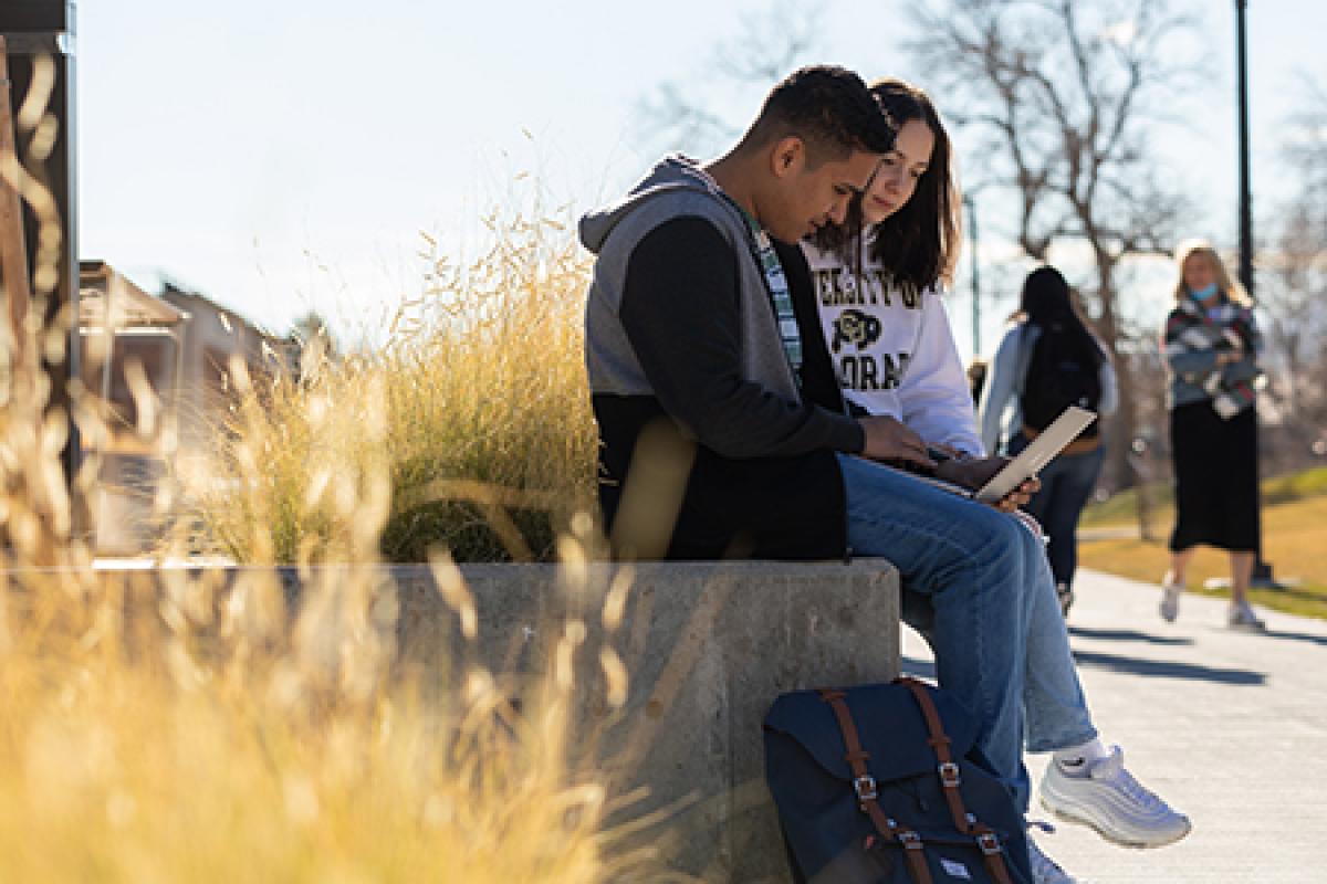 Two students working on a laptop outside Koelbel.