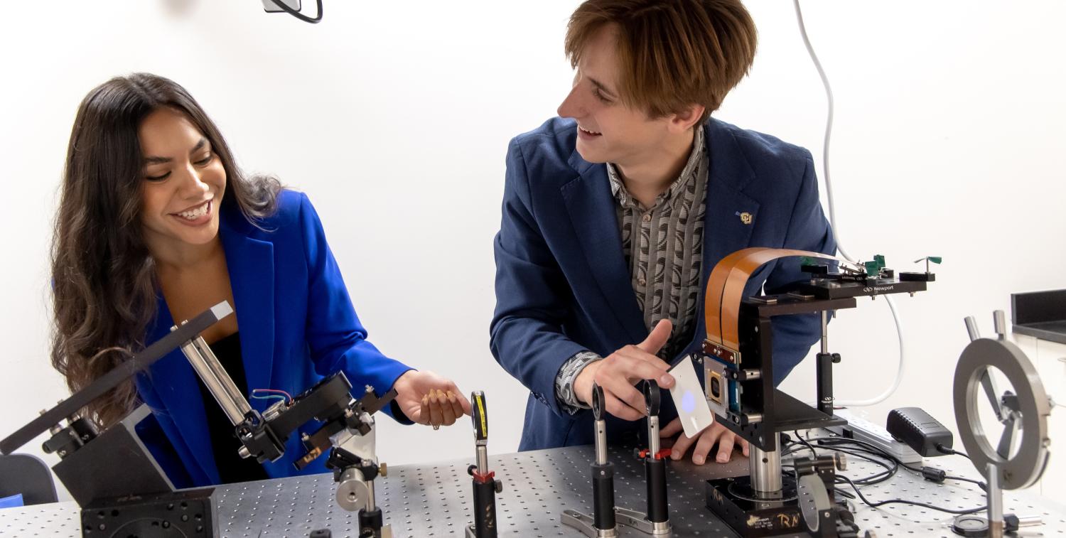 Two students smile while working with technical equipment
